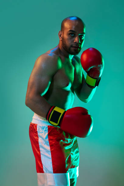 istock Close-up. One professional boxer in red gloves training, exercising over blue green background in neon light. 1330922356
