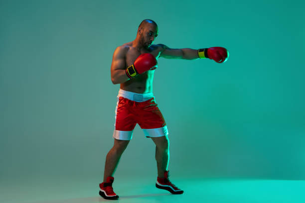 istock Side view. One professional boxer in red gloves training, exercising over blue green background in neon light. 1330922369