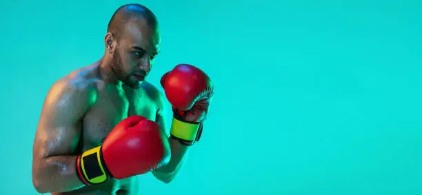 Photo of Flyer. One professional boxer in red gloves training, exercising isolated over blue green background in neon light.