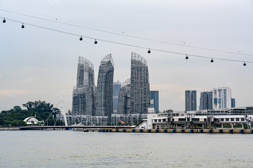 Cable cars passing by over modern skyscraper buildings at the Keppel Bay area in southern Singapore. In front the Pacific Ocean.