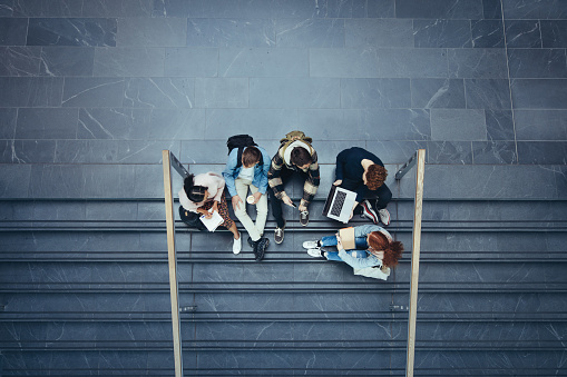 High angle view of students sitting on stairs at college. Young people in high school campus.