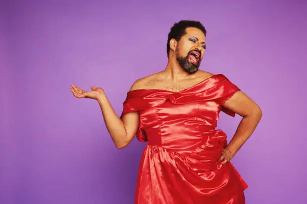 Expressive man in female dress singing. Drag queen wearing makeup and women dress against purple background.