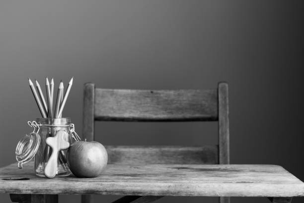 Vintage rustic wood school desk with glass jar of pencils, apple, and small wooden Christian cross on table with copy space.