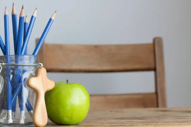 Photo of cross, green apple and pencils on desk with white background