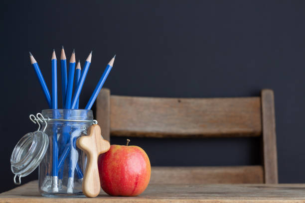 istock cross, red apple and pencils on desk with black background 1330928436