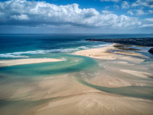 Aerial view over the mouth of the Wallagaraugh River, eastern Victoria, Australia, December 2020, Australia, December 2020 Mallacoota is a small town in the East Gippsland region in the state of Victoria, Australia. At holiday times, particularly Easter and Christmas, the population increases from 1000 to about 10,000. It is the last official township on Victoria's east coast before the border with New South Wales. It is a popular holiday spot for boating, fishing, walking the wilderness coast, swimming, birdwatching, and surfing. tidal inlet stock pictures, royalty-free photos & images