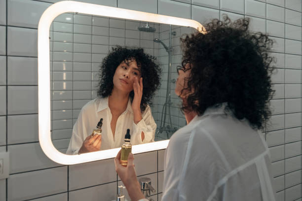 젊은 혼합 인종 여성 부드럽게 현대 욕실에서 손가락얼굴 오일 세럼을 적용. - mirror women bathroom make up 뉴스 사진 이미지