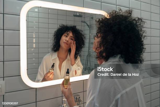 Young Mixed Race Female Gently Applying Face Oil Serum With Fingers In Modern Bathroom Stock Photo - Download Image Now