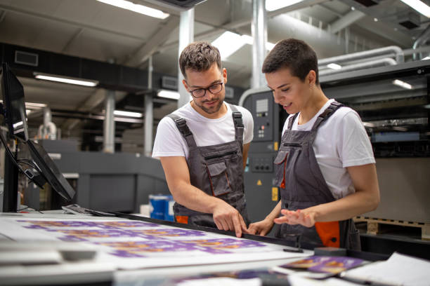 istock Printing machine operators checking graphic quality and color values at print house. 1330930395