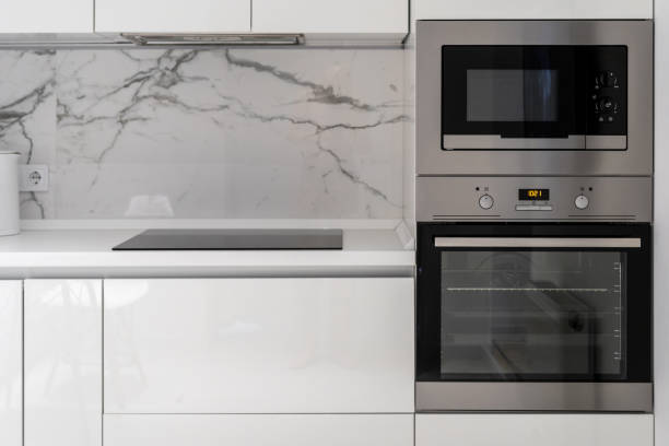 Kitchen counter with electrical plate, oven and microwave Modern kitchen equipment built in white furniture. Induction cooking panel or electical plate on countertop, steel microwave and oven with time display and control knobs for temperature setting. oven door stock pictures, royalty-free photos & images