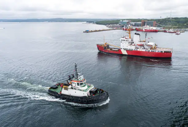 A coast guard ship & tugboat pass in a harbour.