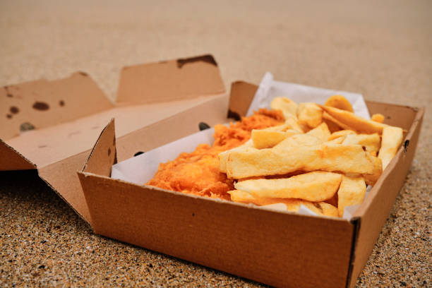 Cardboard box filled  with traditional Fish and Chips on the sand at Newquay, Cornwall on a June day.