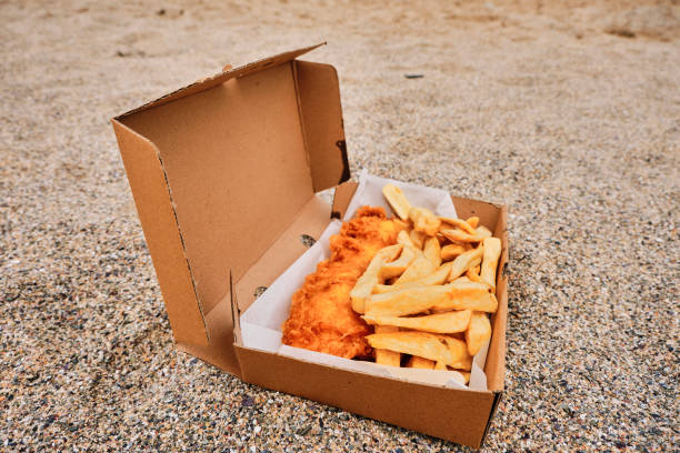 Cardboard box filled  with traditional Fish and Chips on the sand at Newquay, Cornwall on a June day.