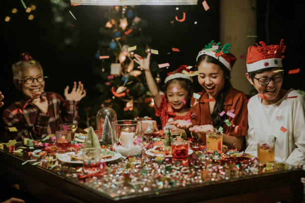 Colorful Confetti paper are falling on Christmas party at night among joyful people - stock photo Thai Multi-generation family celebrating together on New Year's Eve among colorful confetti paper. family christmas party stock pictures, royalty-free photos & images