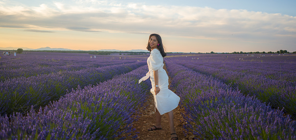 outdoors romantic portrait of young happy and attractive woman in white summer dress enjoying carefree at beautiful lavender flowers field in travel and holiday concept