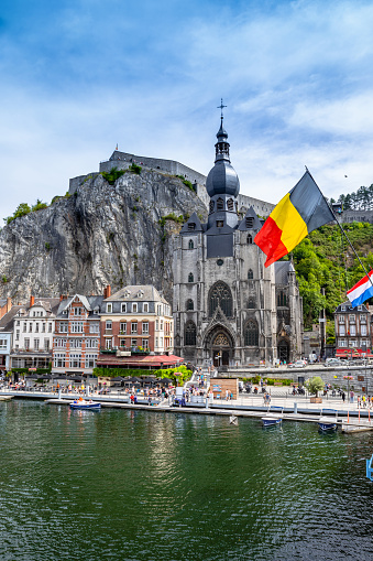 The historic town of Dinant with the Belgian flag and the citadelle on the rock and Collegiate Church of Notre-Dame at the Meuse river, Wallonia, Belgium