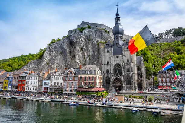 The historic town of Dinant with the Belgian flag and the citadelle on the rock and Collegiate Church of Notre-Dame at the Meuse river, Wallonia, Belgium