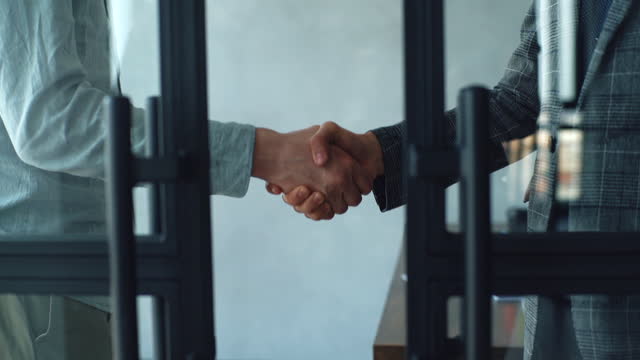 Close-up hands of unrecognizable business partners shaking hands agree to deal or say hello in office on background of glass door.