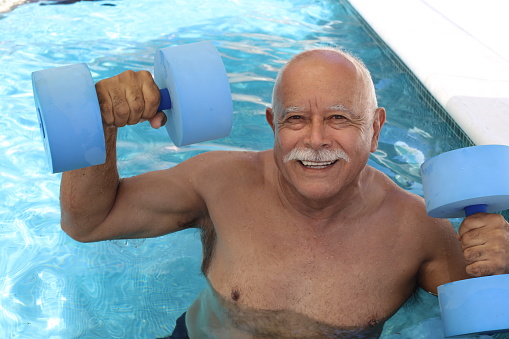 Senior man holding dumbbells in swimming pool.