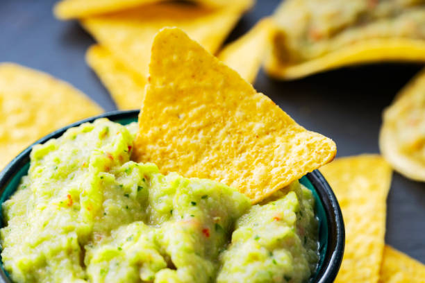 istock Guacamole and nachos chips on a dark background. Guacamole sauce with corn chips on a slate board. Close-up. Selective focus 1330955658