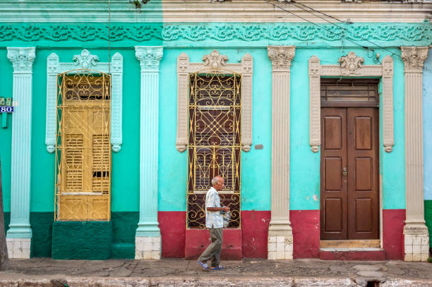 senior man walking down a street in Trinidad, Cuba August 8, 2018 - Trinidad, Cuba: old local senior man walking down a street in Trinidad in front of a traditional house, Cuba trinidad culture stock pictures, royalty-free photos & images
