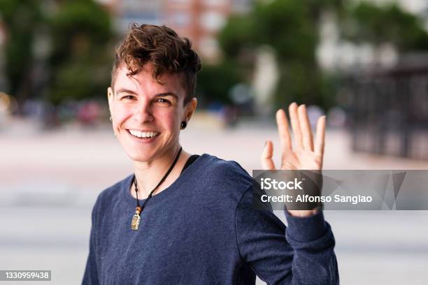 Non Binary Transgender Tomboy Looking At Camera Greeting And Waving Hand Smiling During Internet Online Communication Stock Photo - Download Image Now