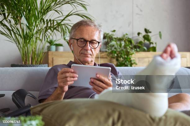 Senior Man With Broken Leg At Home Stock Photo - Download Image Now - Physical Injury, Watching TV, Orthopedic Cast