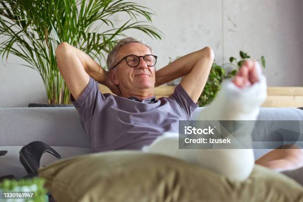 Senior Man With Broken Leg At Home Stock Photo - Download Image Now - Orthopedic Cast, Broken Leg, Sofa