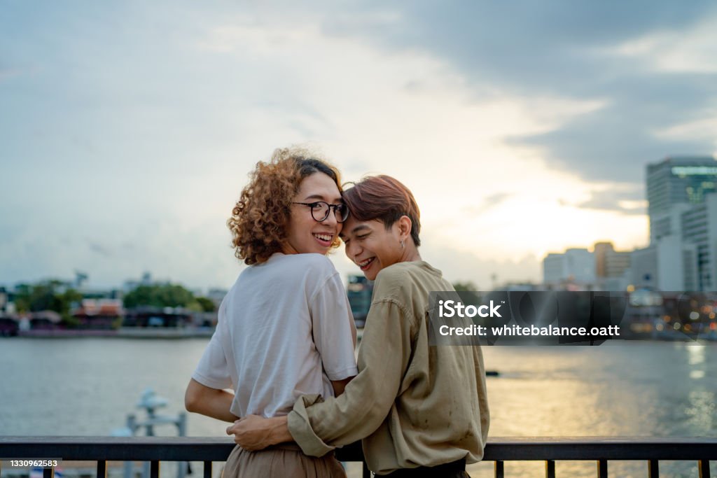 LGBTQIA couple resting at waterfront. Lovely Asian couple having fun and embracing, loving each other on holiday. Non-Binary Gender Stock Photo