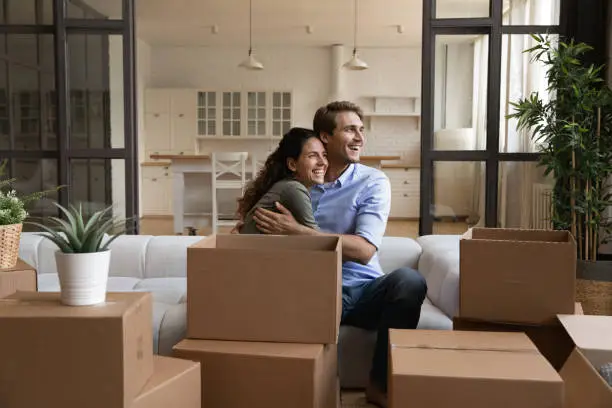 Full of ideas and plans. Happy married couple new homeowners of comfortable apartment hug on sofa at relocation day dream of future. Inspired young spouses take break in unboxing things relax together