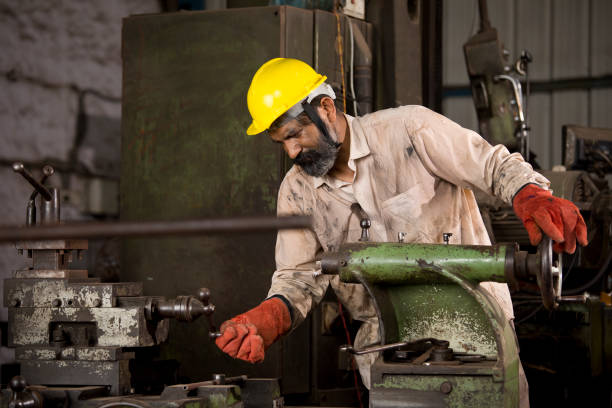 Engineer using lathe in workshop Engineer in protective workwear inspecting lathe at factory helmet hardhat protective glove safety stock pictures, royalty-free photos & images