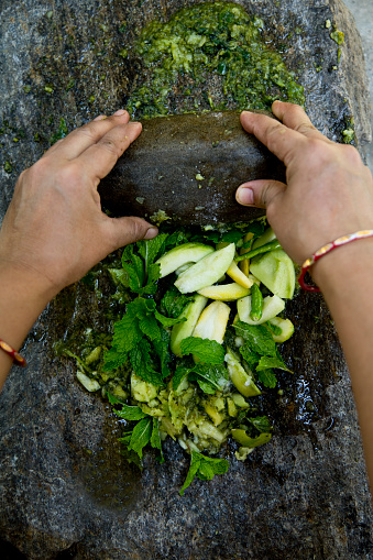 Woman hands grinding fresh mint leaves with garlic and chillies on stone grinder