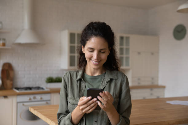 istock Young lady look at phone screen chat online at kitchen 1330962937