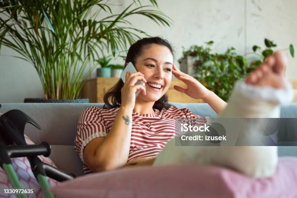 Cheerful Young Woman With Broken Leg On Phone Stock Photo - Download Image Now - Physical Injury, Broken Leg, Orthopedic Cast