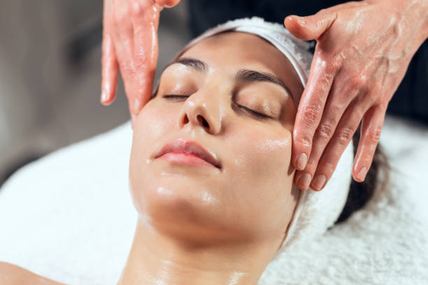 cosmétologue faisant massage du visage pour le rajeunissement à la femme tout en étant allongé sur une civière dans le centre de spa. - esthéticienne photos et images de collection