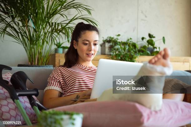 Young Woman With Broken Leg At Home Stock Photo - Download Image Now - Laptop, Orthopedic Cast, Broken Leg