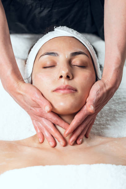 cosmetologo che fa massaggio viso per ringiovanimento alla donna mentre giace su una barella nel centro termale. - massaging facial massage beautician beauty treatment foto e immagini stock