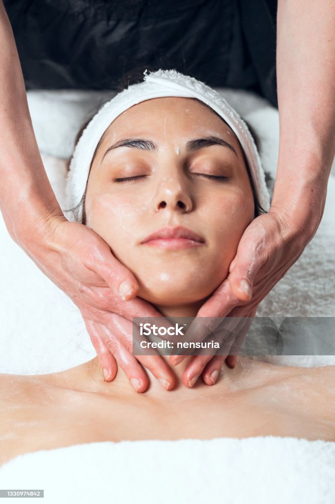 Cosmetologist making face massage for rejuvenation to woman while lying on a stretcher in the spa center. Shot of cosmetologist making face massage for rejuvenation to woman while lying on a stretcher in the spa center. Facial Mask - Beauty Product Stock Photo