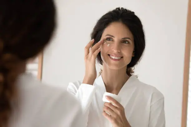 Photo of Smiling young hispanic woman apply nourishing cream under eyes