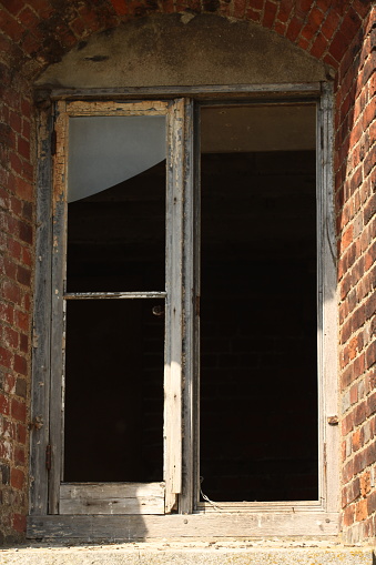 An old wooden window frame with broken windows and flaking paint looking into a dark room