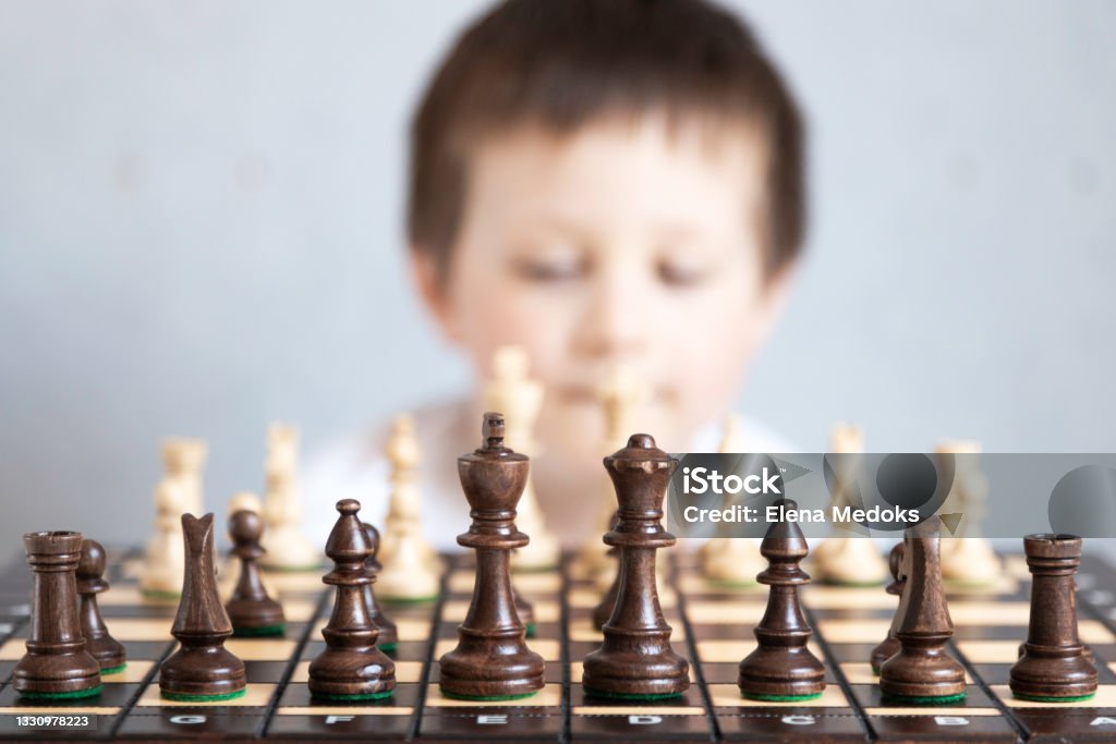 A chessboard with spaced figures, in the background a boy out of focus. Board game of chess. Tournaments and schools for young chess players A chessboard with spaced figures, in the background a boy out of focus. Board game of chess. Tournaments and schools for young chess players. Child Stock Photo