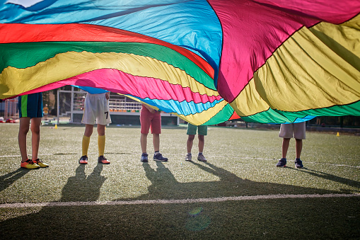 Grupo de amigos jugando y agitando paracaídas de colores brillantes, fiesta al aire libre, campamento de la escuela de verano photo