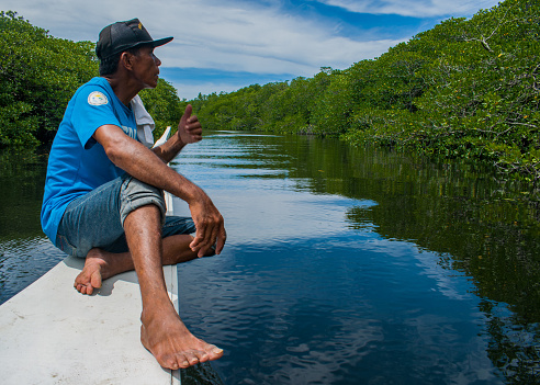 A village watchman on a boat in the middle of a mangrove estuary. Pre-Covid.