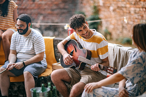 Photo of  young man play acoustic guitar on party in a backyard.