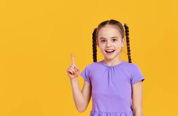 istock Happy   kid girl  pointing up while standing in yellow studio 1330984037