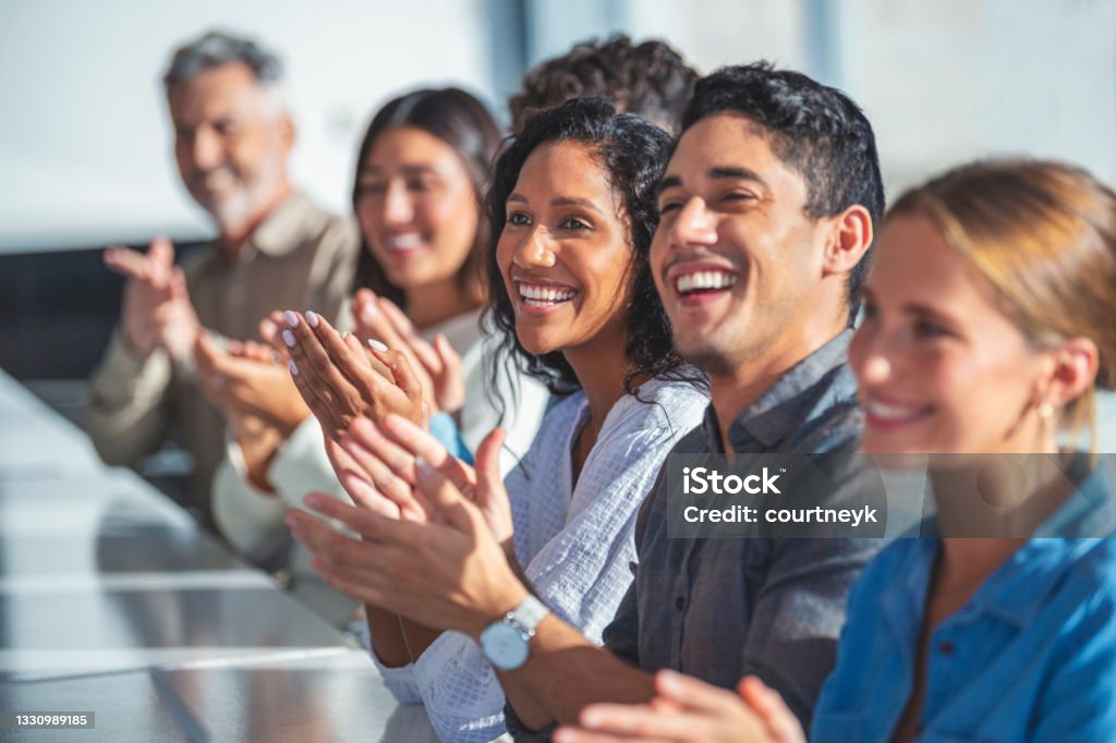 Group of business people applauding a presentation. Group of business people applauding a presentation. They are sitting at a table in a sunny room. There are several ethnicities present including Caucasian, African and Latino Celebration Stock Photo