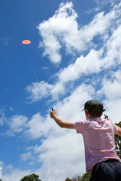 A young boy flies a stunt kite at the beach in summer.