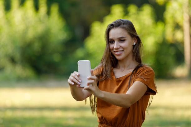 istock A Young Woman is Using a Mobile Phone to Make Self Portrait Photo While Walking in a Park. 1330993149