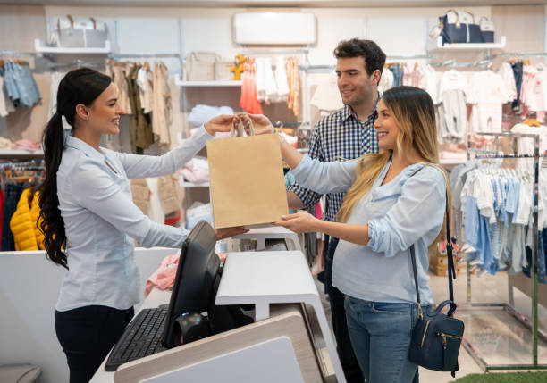 Couple expecting a baby and shopping for clothes at a store Couple expecting a baby and shopping for clothes at a store while paying at the cashier and getting a bag - lifestyle concepts baby boutique stock pictures, royalty-free photos & images