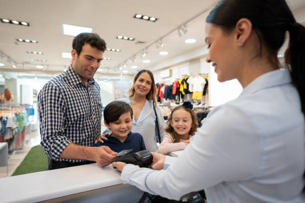 Happy family shopping and paying by card at a kids clothing store Happy Latin American family shopping and paying by card to the cashier at a kids clothing store - retail concepts clothing store credit card stock pictures, royalty-free photos & images